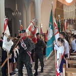 Wymaszerujący poczet sztandarowy wojska polskiego na tle pocztów szkolnych.