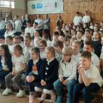 Dzieci siedzące na sali gimnastycznej podczas apelu.