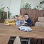 Trójka uczniów siedząca przy stole, trzymająca banknot.