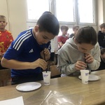 Uczniowie za pomocą słomki przenoszą papierowe kółka do kubeczka.