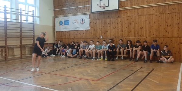 Grający uczeń klasy 7 na tle grupy czekającej na swoje mecze w Mikołajkowym Turnieju Badmintona.